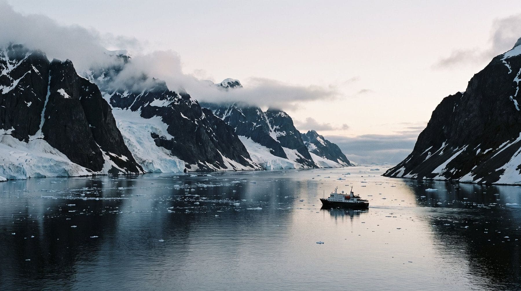 A small expedition ship dwarfed by the black rock and snow walls of the Lemaire Channel