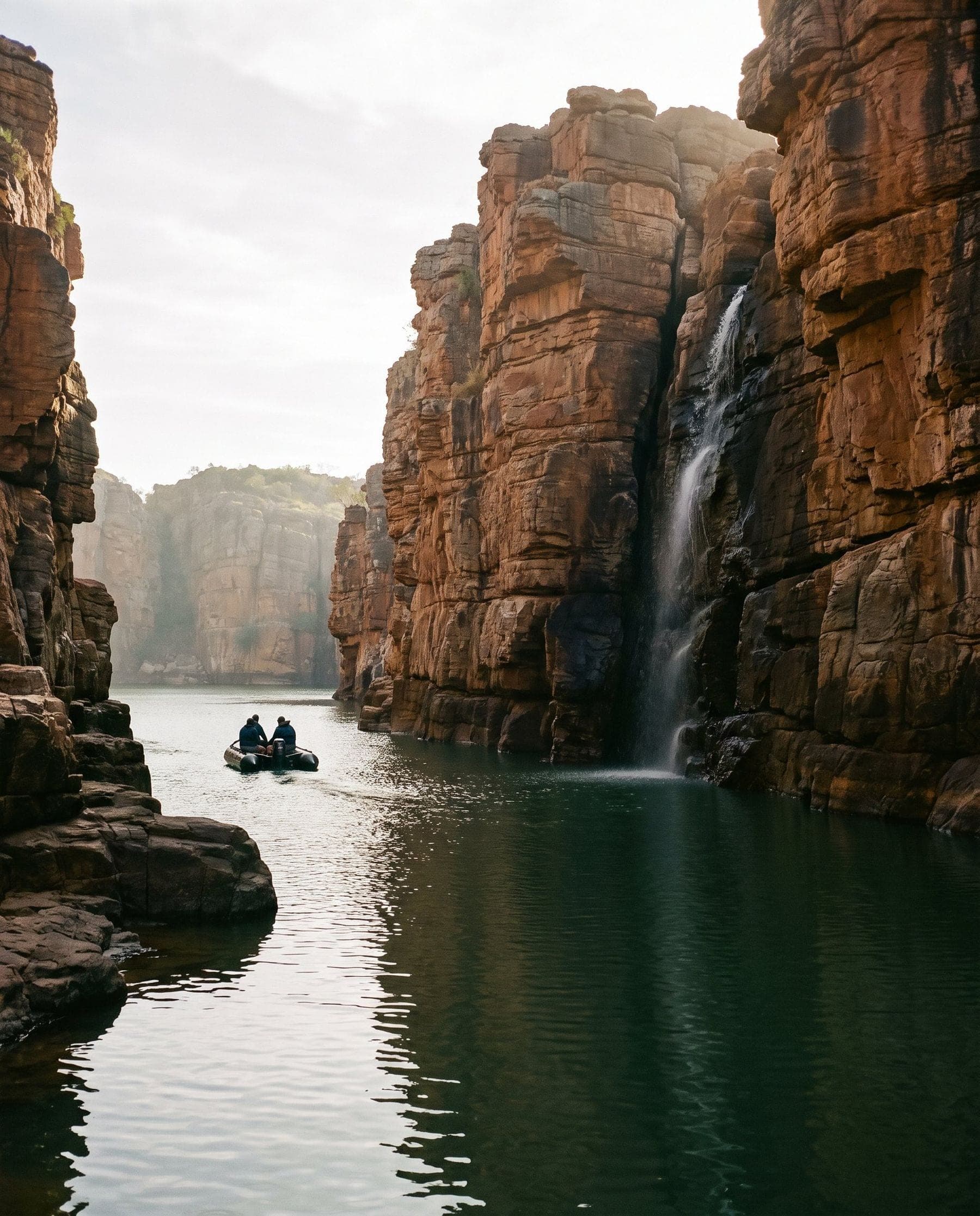 Red sandstone cliffs and a waterfall in a tidal gorge on the Kimberley coast, with a small tender on the water
