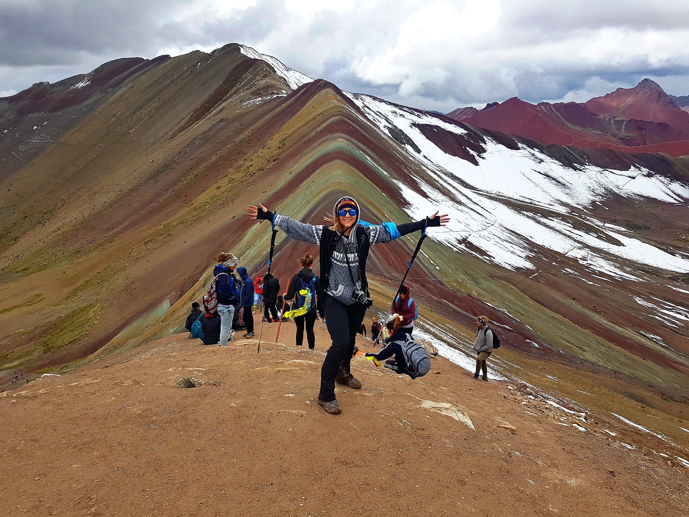 Walkers on the ridge at Vinicunca, the striped red, ochre and green slopes of Rainbow Mountain behind them