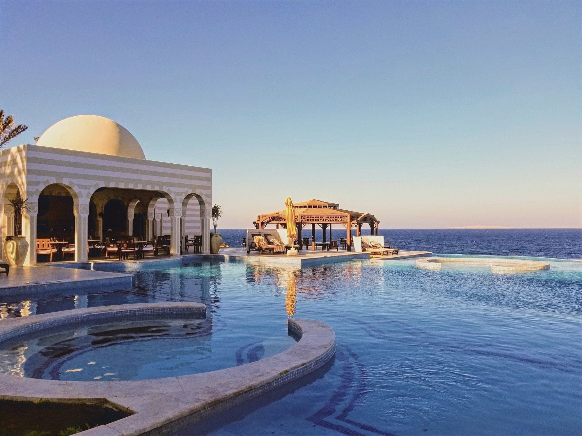 A domed pavilion and pool spilling toward the Red Sea under a clear evening sky