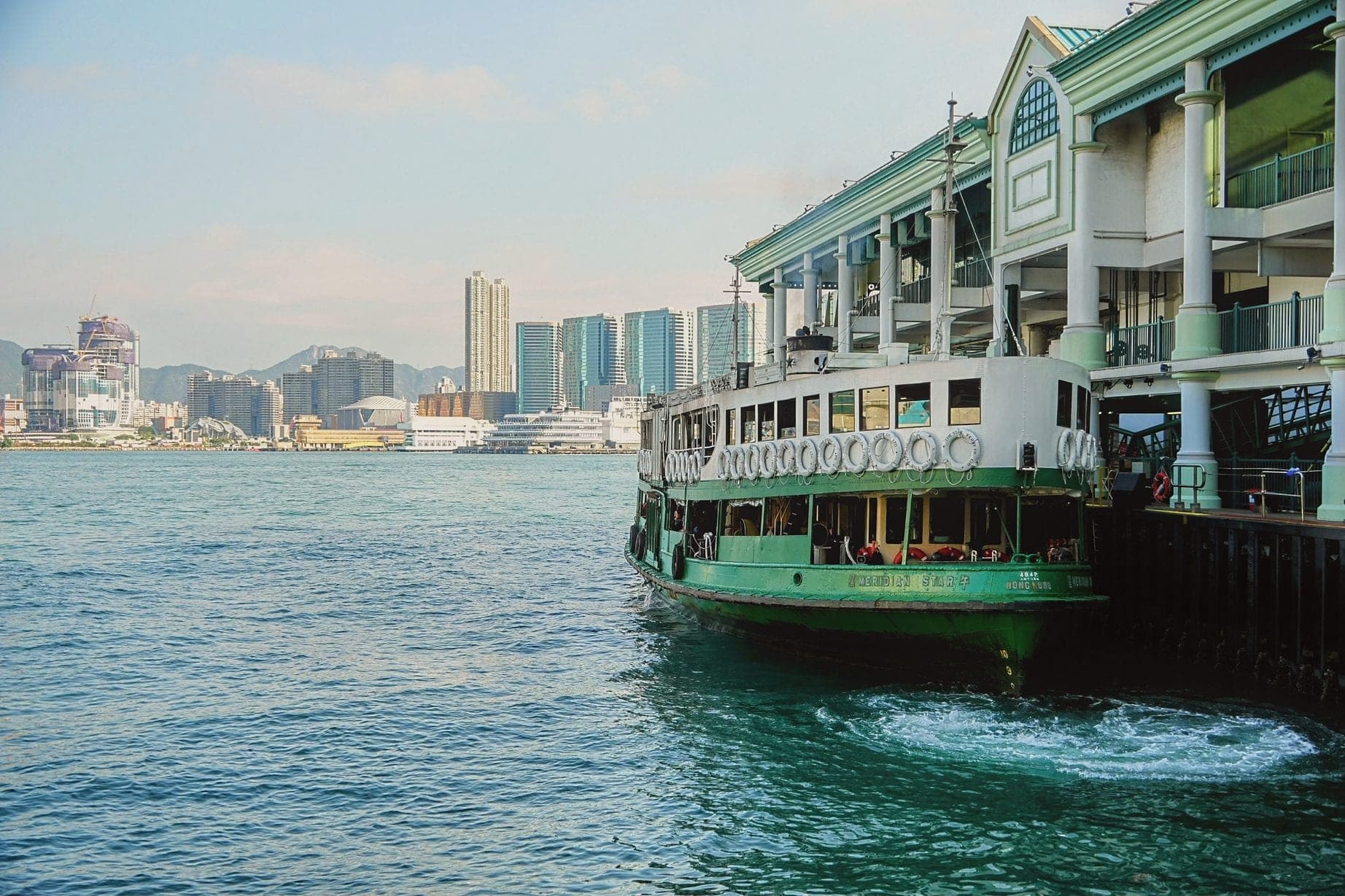 A green and white Star Ferry pulling away from the pier, Hong Kong skyline behind