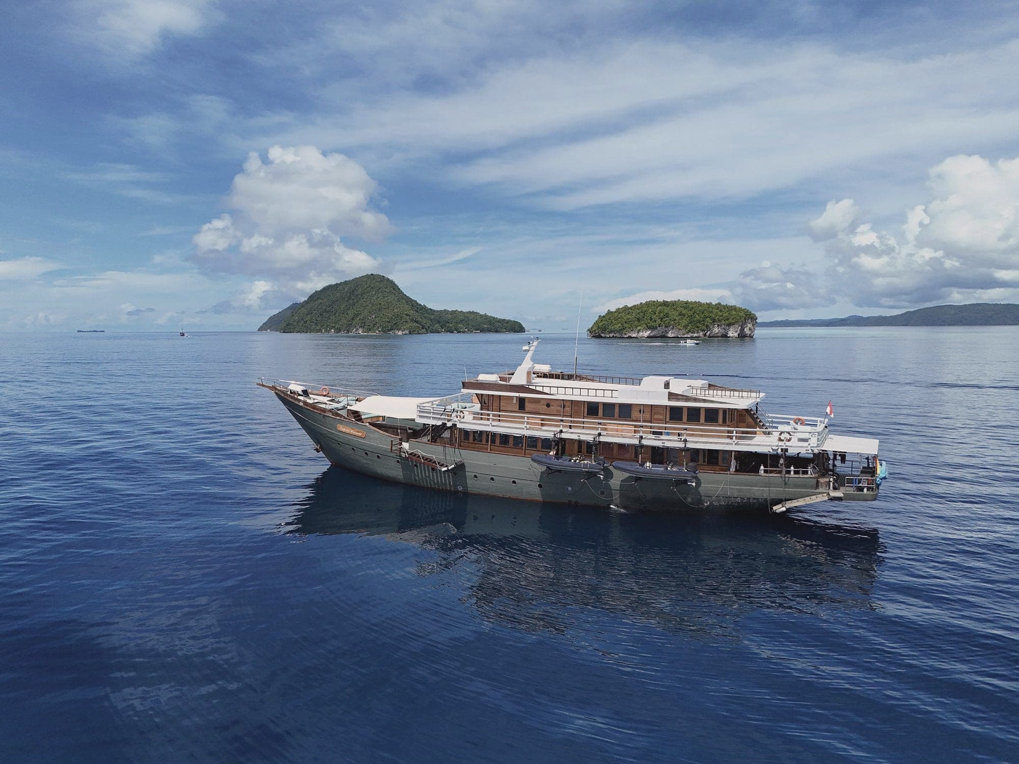 The phinisi Emperor Harmoni at anchor on calm blue water between two small islands