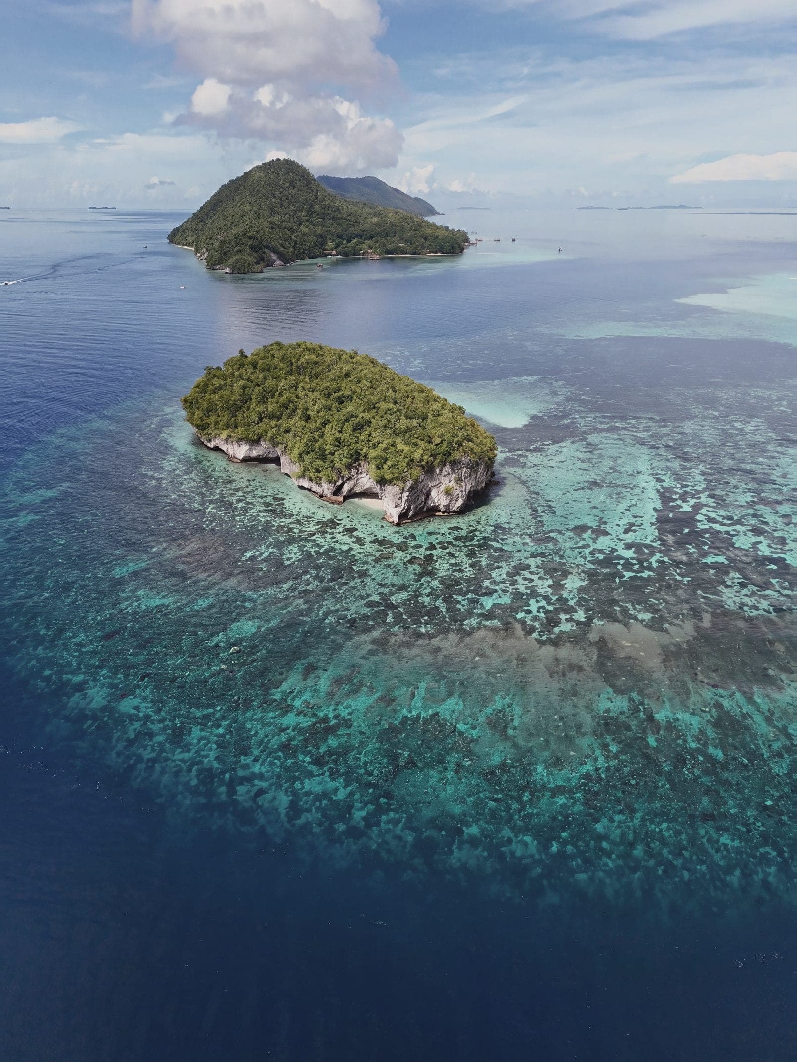 Two small islands above a wide reef flat in clear water, seen from the air