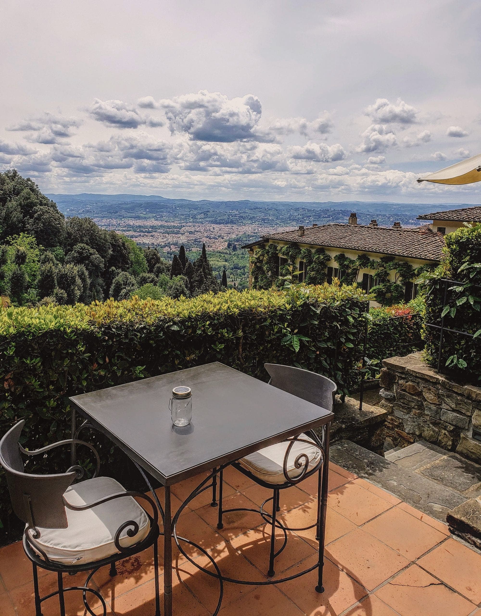 A wrought iron table and chairs on a hedged terrace looking out over the valley toward Florence