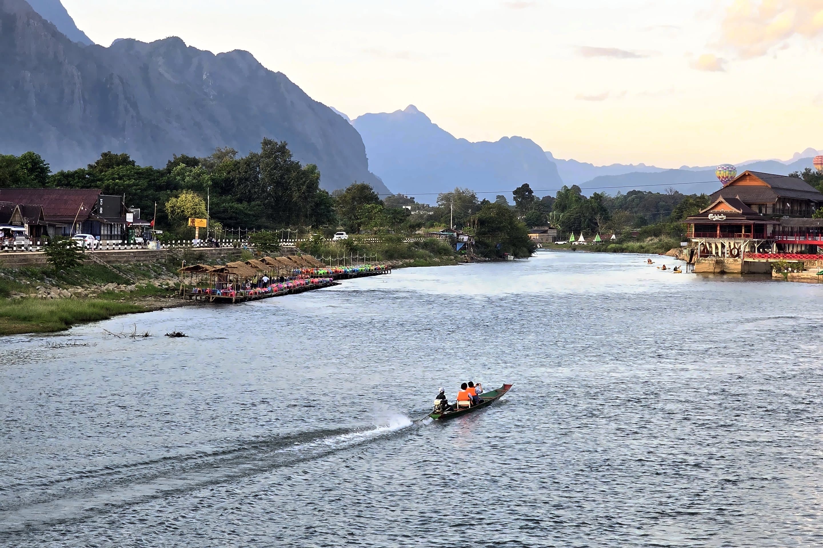A longtail boat on a river below karst mountains at dusk, Laos