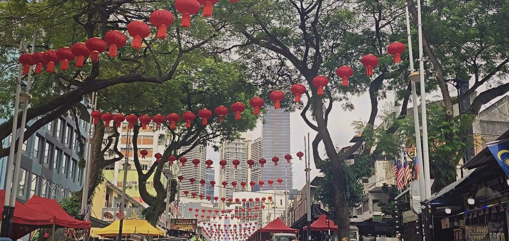 A Kuala Lumpur street hung with red lunar new year lanterns, towers behind