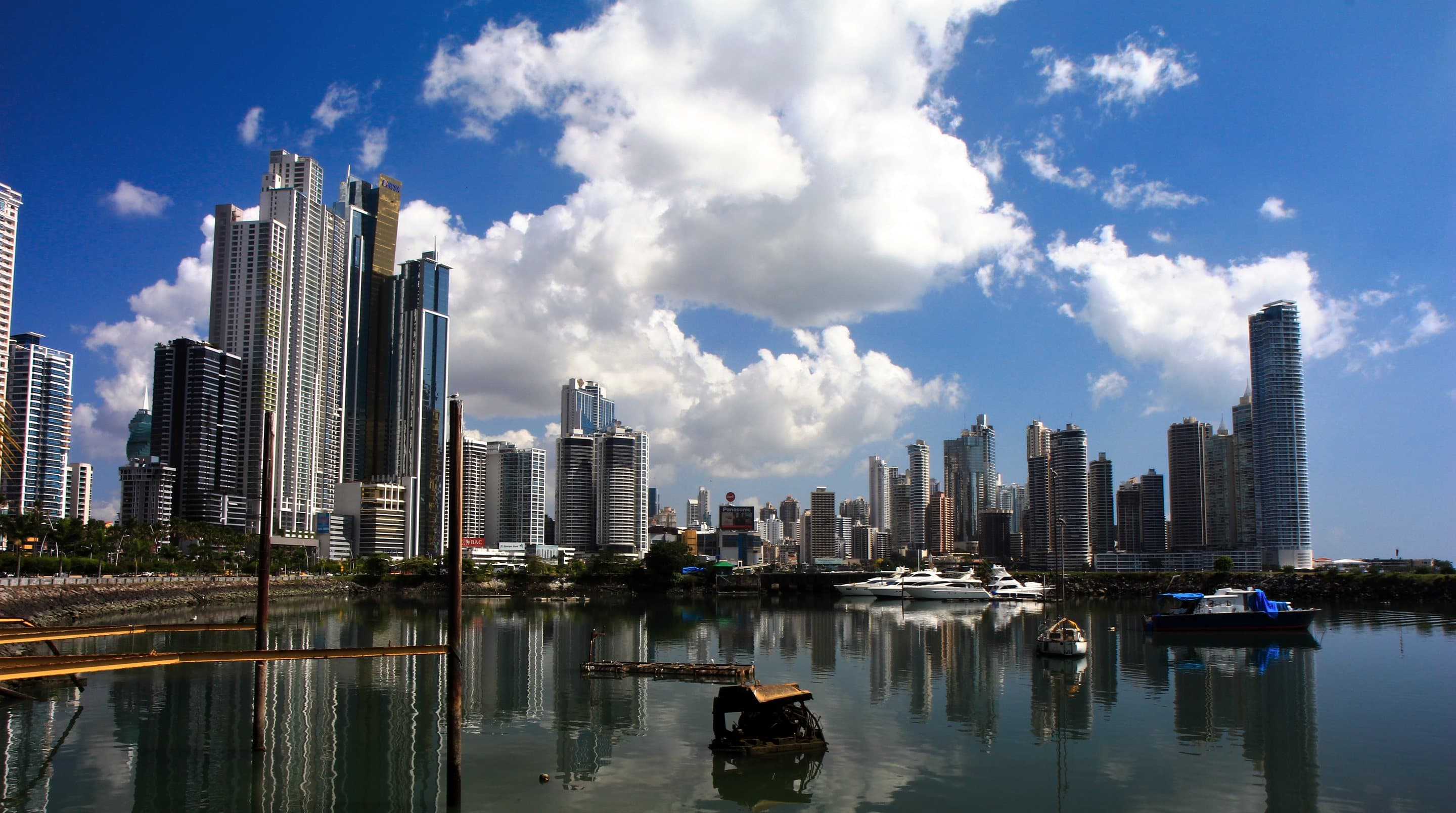 The towers of modern Panama City reflected in the calm water of the bay under white cloud