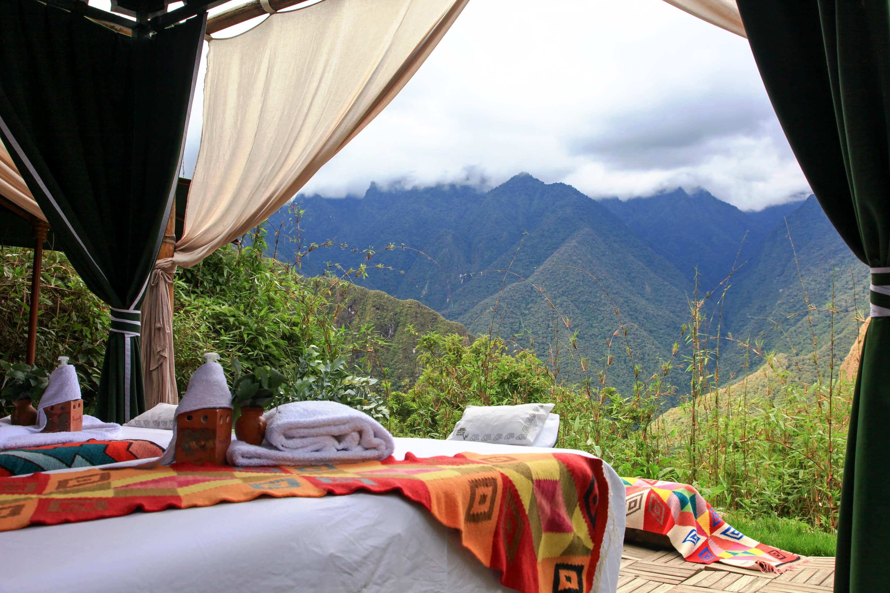 An open terrace pavilion with curtains and two treatment beds facing the green mountains of the Urubamba gorge