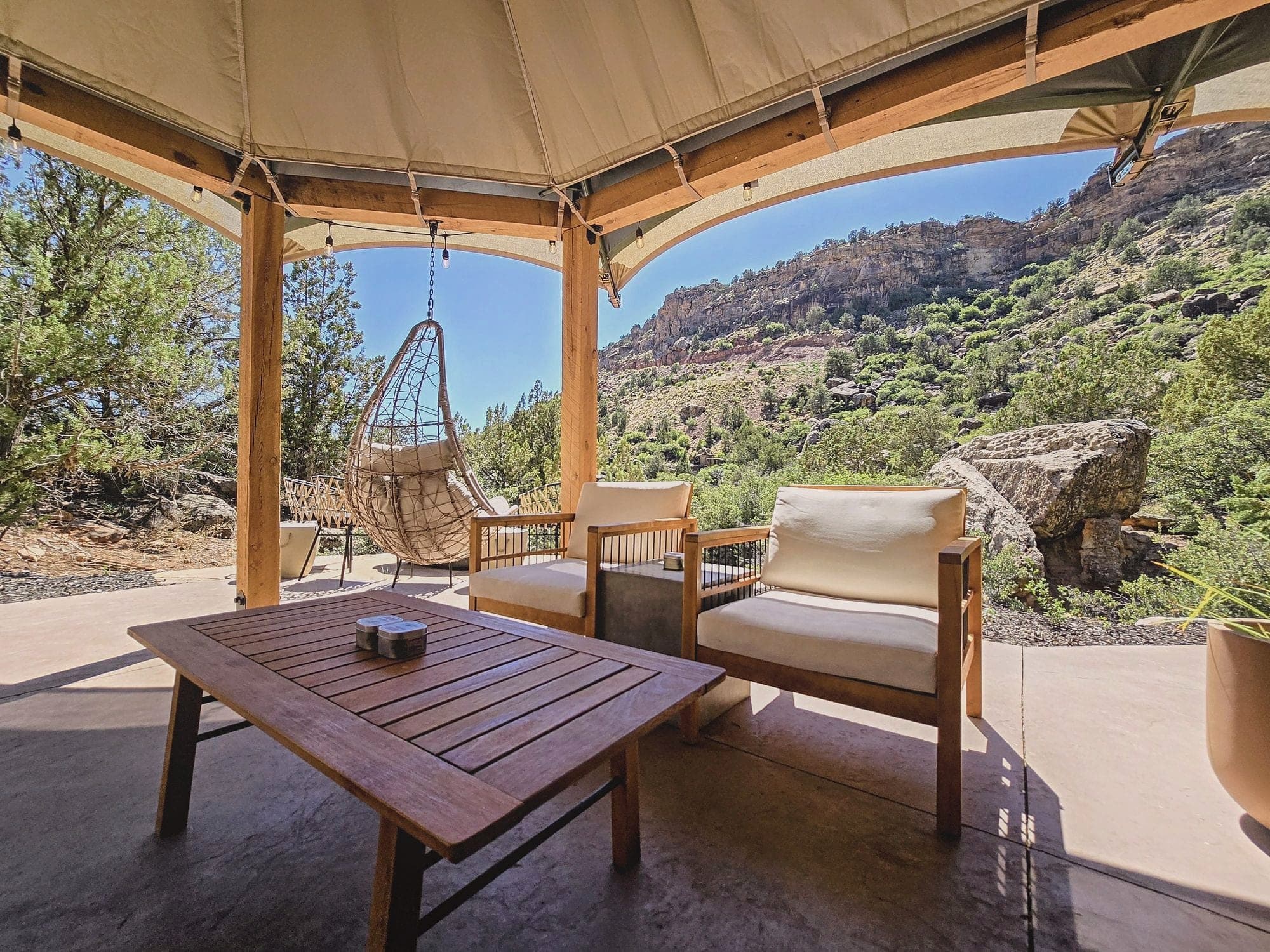 A covered patio with a hanging chair and armchairs looking out over a desert canyon