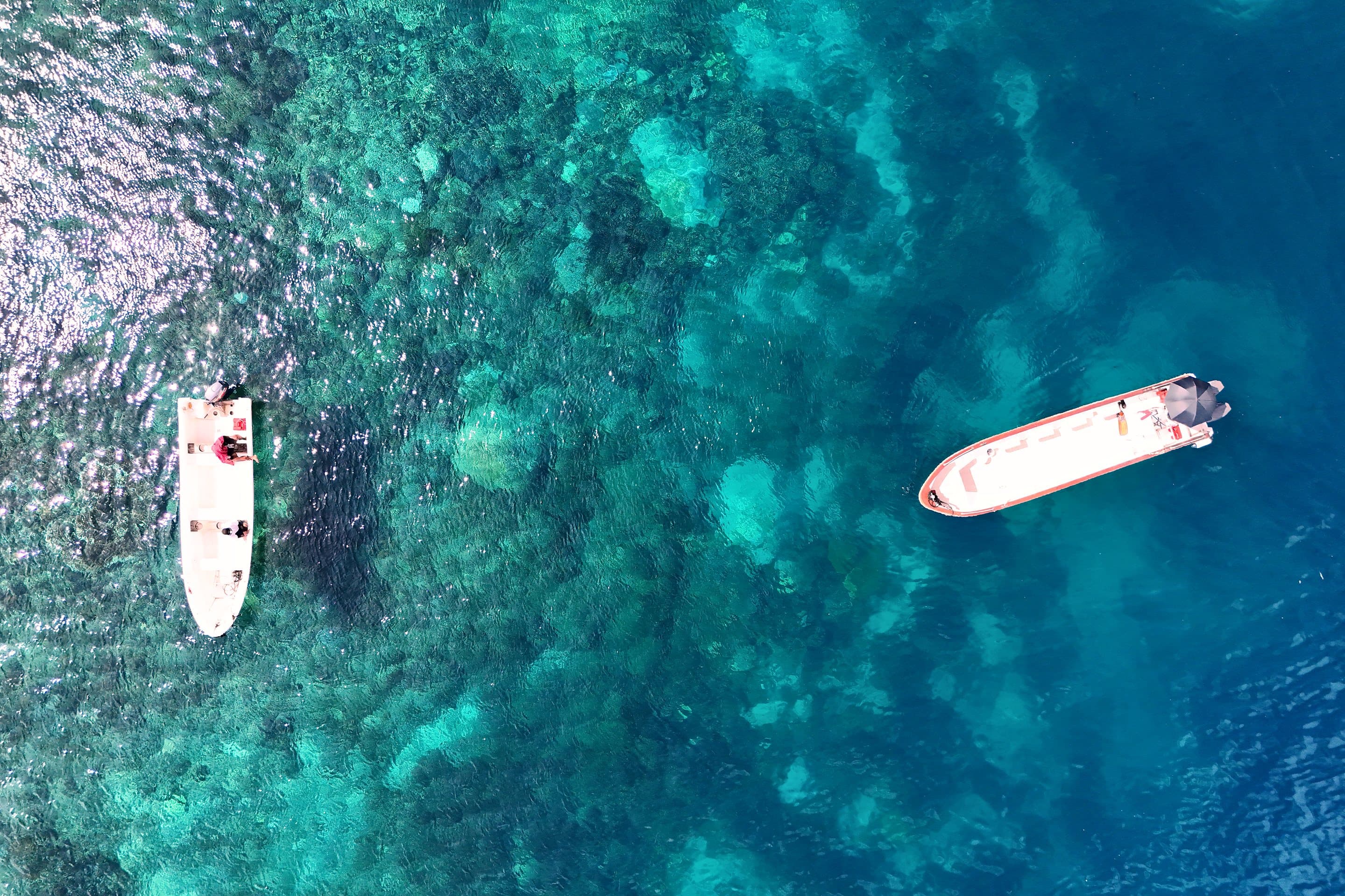 Two boats over turquoise reef water in Raja Ampat, Indonesia, seen from above