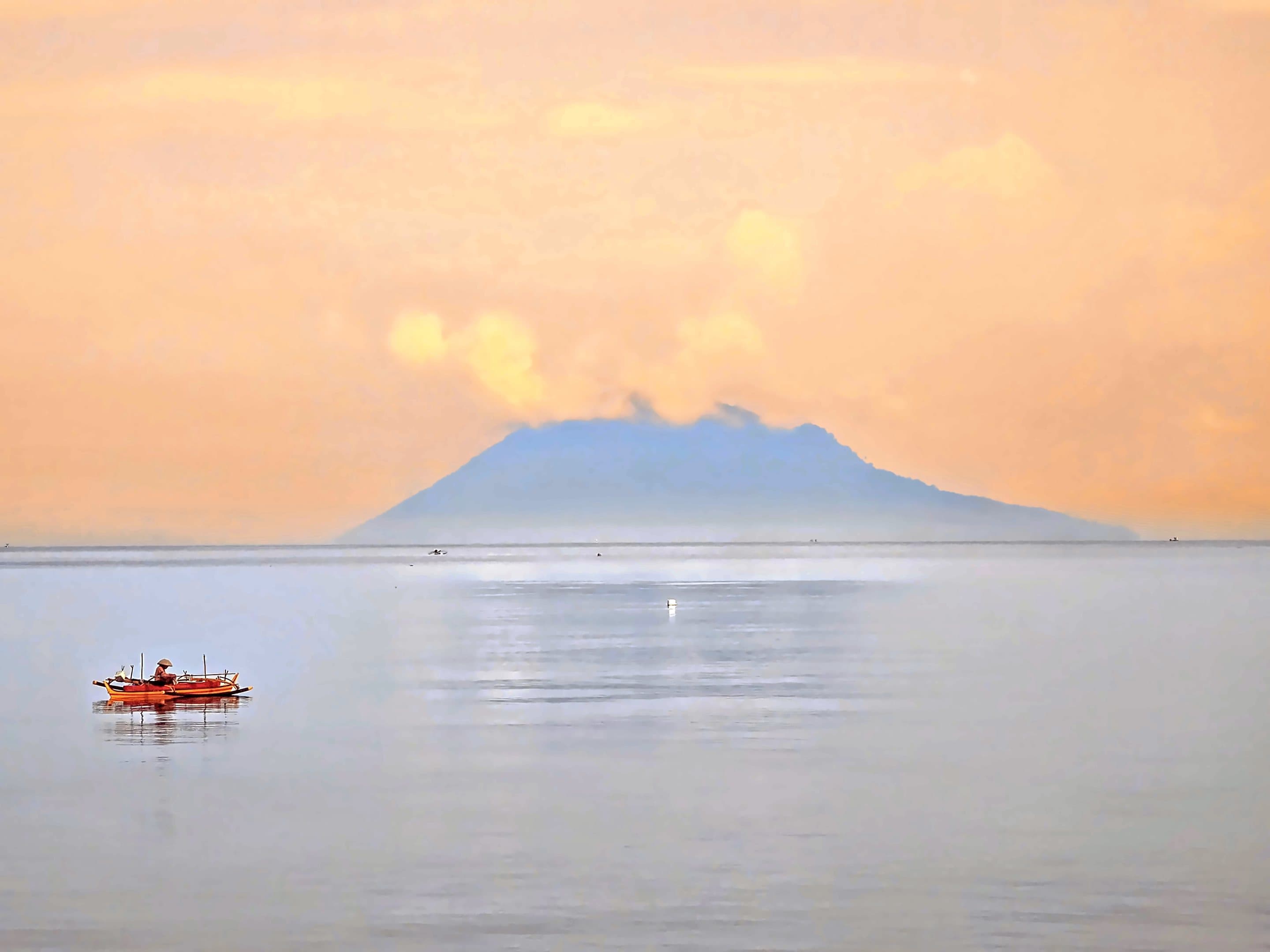A lone outrigger on a still sea at dawn below the Manado Tua volcano, North Sulawesi